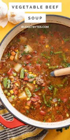 a pot filled with vegetable beef soup on top of a yellow table cloth next to garlic