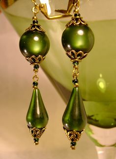 a pair of green earrings sitting on top of a glass vase next to a wine glass