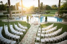 an outdoor ceremony setup with white chairs and flowers on the aisle, surrounded by palm trees