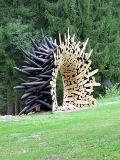 a large sculpture made out of logs in the middle of a field with trees behind it