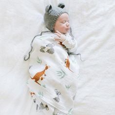 a newborn baby wrapped in a blanket and wearing a knitted hat with animals on it