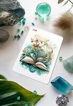 a playing card surrounded by crystals and other items on a white table with green leaves