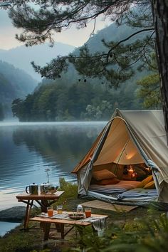 a tent is set up on the shore of a lake with two tables and chairs