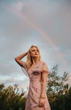 a woman in a pink dress standing under a rainbow