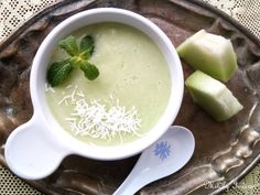 there is a bowl of soup with cucumber and mint on the side