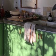 a kitchen with green cabinets and white counter tops is pictured in this image, the sunlight shines through the window onto the dishwasher