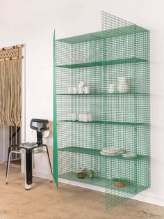 a green shelf filled with dishes next to a chair