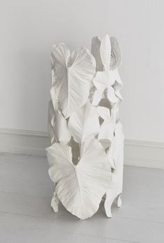 a white sculpture sitting on top of a floor next to a wall with flowers growing out of it