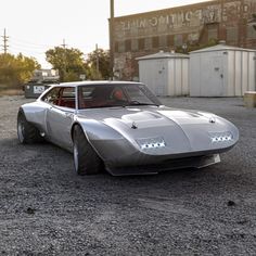 a silver car parked in front of an old brick building on gravel road next to power plant