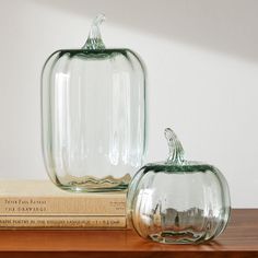 two glass pumpkins sitting on top of a wooden table next to an open book