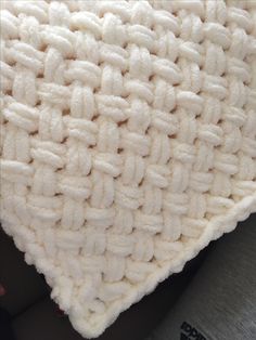 a close up view of a white knitted blanket on someone's lap,