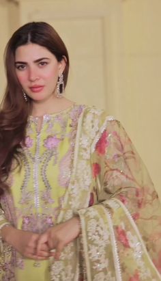 a woman with long hair wearing a yellow dress and matching white jewelry stands in front of a wall