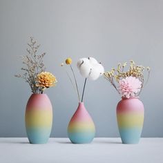 three vases with flowers in them sitting on a table next to each other,