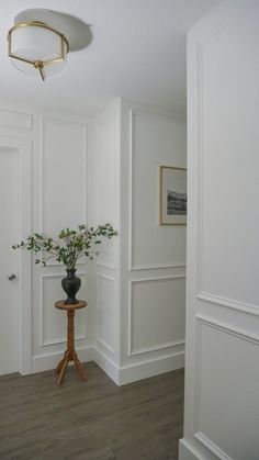 a room with white walls and wood flooring has a plant on the end table