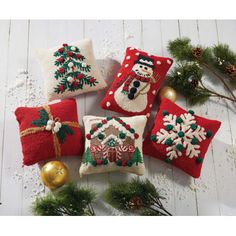 four red christmas pillows with snowmen and trees on them, sitting next to evergreen branches