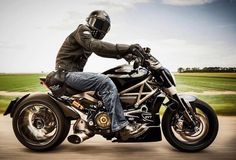 a man riding on the back of a motorcycle down a road with grass in the background