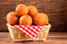 a basket filled with lots of doughnuts on top of a wooden table next to a red and white checkered napkin