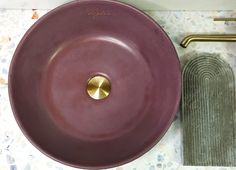 a purple sink sitting on top of a counter next to a green towel and gold faucet