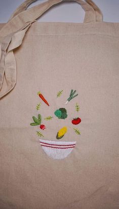 a tote bag with embroidered vegetables and carrots in a bowl on the side