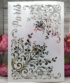 a white card with gold foil on it and some pink flowers in front of it