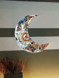 a mosaic moon hanging on the wall next to a vase with dried flowers in it