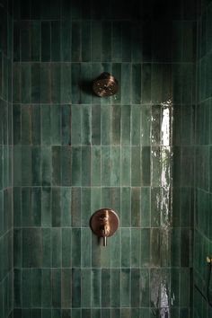 two copper faucets are mounted on the green tiled shower wall in this bathroom