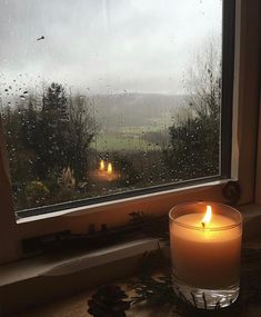 a candle sitting on top of a window sill in front of a rain soaked window