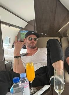 two men are sitting on an airplane with drinks and water in front of their faces