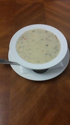 a white bowl filled with soup on top of a wooden table next to a spoon