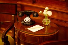 an old fashioned telephone sitting on top of a table next to a vase with flowers