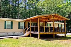 a mobile home with a covered porch in front of it and trees surrounding the house