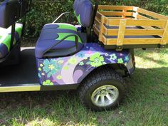 a purple and green golf cart with flowers painted on the side, sitting in grass