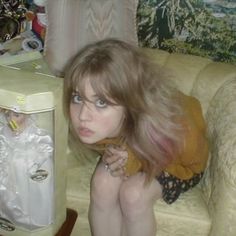 a woman sitting on a couch next to an old fashioned refrigerator with a doll in it