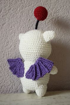 a crocheted stuffed animal with purple wings and a red flower in its mouth