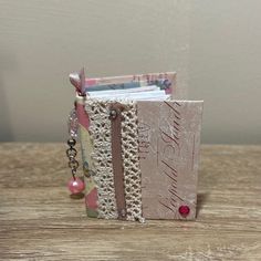 a small book is sitting on top of a wooden table and has beads hanging from it