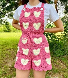 a woman wearing pink and white crocheted overalls with hearts on the front