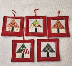 four christmas tree ornaments hanging from red frames on a white sheet with snowflakes