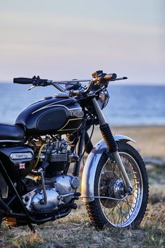 a black motorcycle parked on top of a grass covered field next to the ocean in front of a blue sky