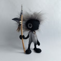 a black and white stuffed animal holding a wooden stick with feathers on it's head