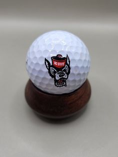 a white golf ball sitting on top of a wooden stand next to a black and red logo