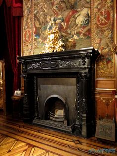 an ornate fireplace in the middle of a room with tapestry on the wall behind it