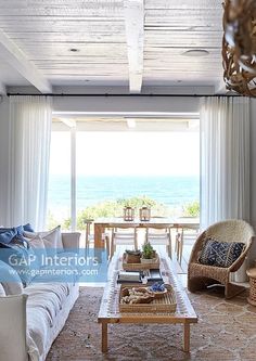 a living room filled with furniture and a large window covered in curtains over the ocean