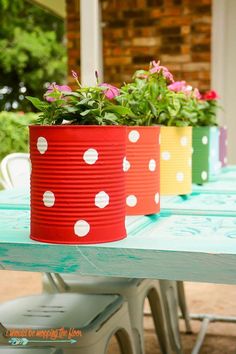 three colorful tin can planters sitting on top of a blue picnic table with flowers in them