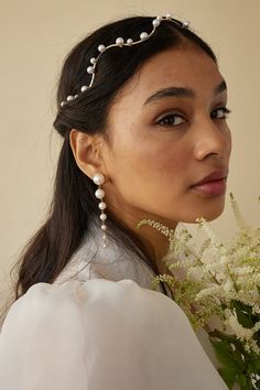 a woman in a white dress holding flowers and wearing a headband with pearls on it