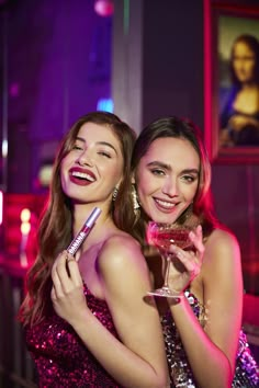 two beautiful young women standing next to each other holding wine glasses in front of their faces