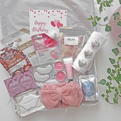 the contents of a birthday hamper are laid out on a white surface with pink flowers