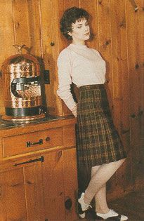 a woman standing in front of a wooden wall with a coffee pot on the stove