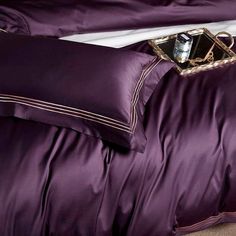 a bed with purple comforter and pillows on top of it, next to a pillow case