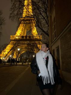 a woman is walking down the sidewalk in front of the eiffel tower at night