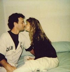 a man and woman sitting on top of a bed next to each other, kissing